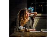Girl rubs neck at table with tea or coffee.